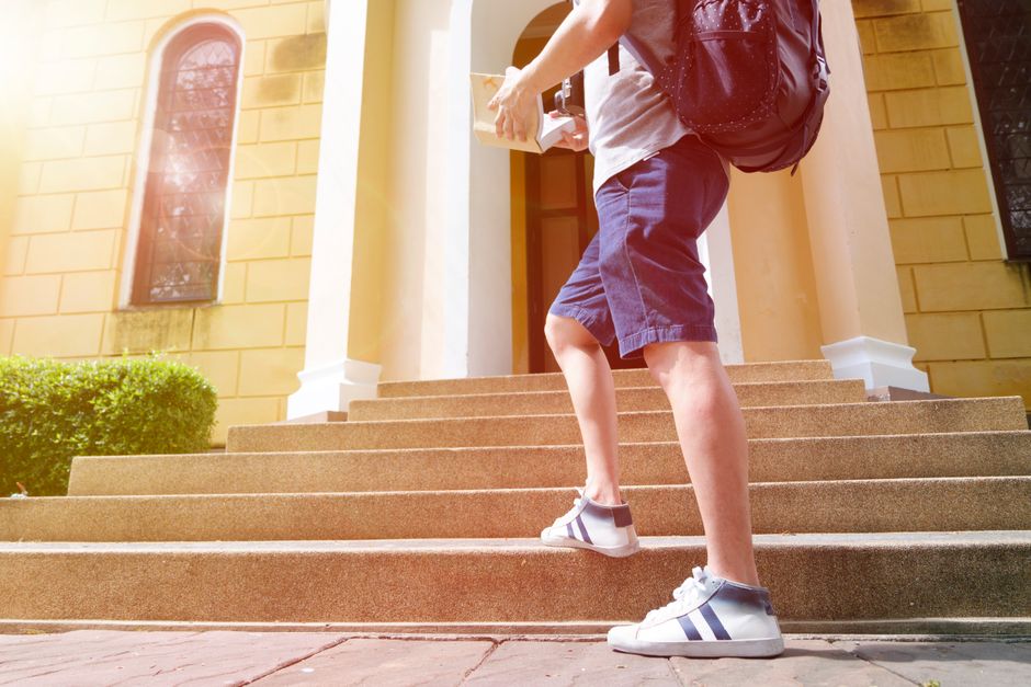 A young man with a backpack climbs steps to a historic building on a sunny day.